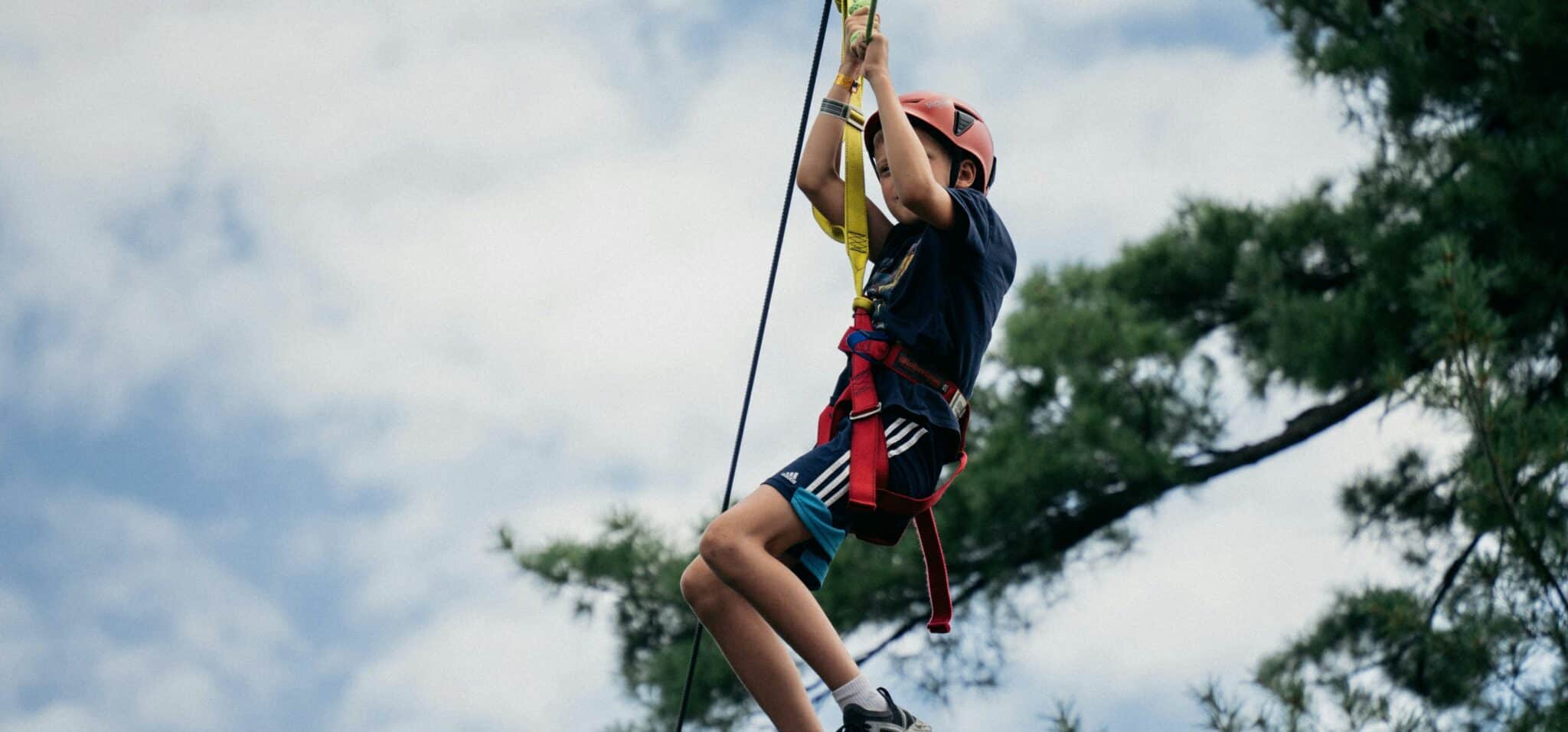child zip lining with tree and sky in the background